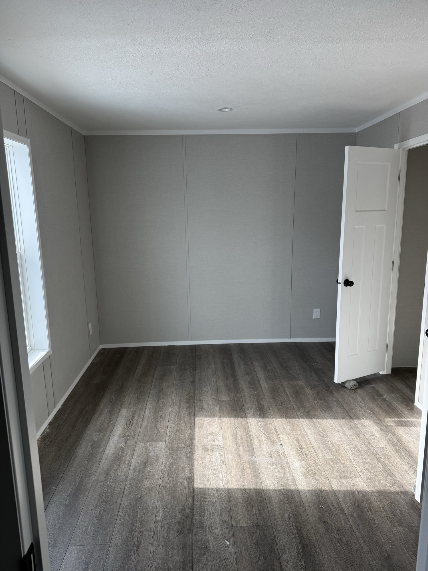 New manufactured home bedroom — Limestone community, Finger Lakes NY. Hardwood-style flooring, gray walls, natural light from a side window.